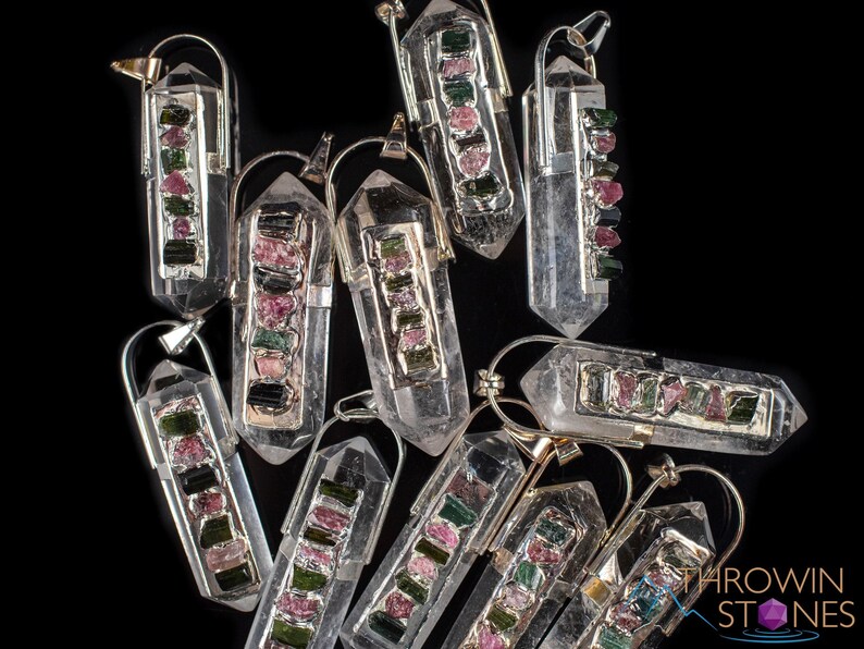 This crystal pendant features a clear Quartz gemstone, showcasing its transparent beauty and amplifying properties. Surrounding the Quartz are seven, green and pink Tourmaline gemstone accent crystals.