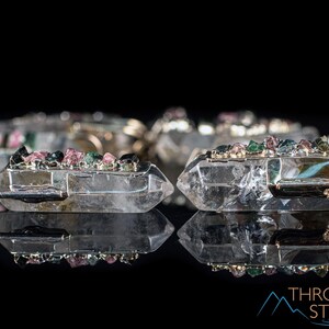 This crystal pendant features a clear Quartz gemstone, showcasing its transparent beauty and amplifying properties. Surrounding the Quartz are seven, green and pink Tourmaline gemstone accent crystals.