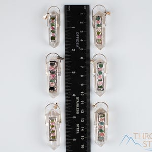This crystal pendant features a clear Quartz gemstone, showcasing its transparent beauty and amplifying properties. Surrounding the Quartz are seven, green and pink Tourmaline gemstone accent crystals.