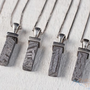 May include: Four rectangular pendants with a textured, dark gray pattern are displayed on silver chains. Each pendant is attached to a silver bail. The pendants are arranged on a white wooden surface. The logo "Thrown Stones" is visible in the bottom right corner.