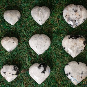 Genuine Moonstone heart shaped crystal. This beautifully hand carved, puffy, palm stone heart, is white with specks of black and rainbow flash. Each crystal heart is unique, and has its own color, shape, and pattern. This listing has variations.