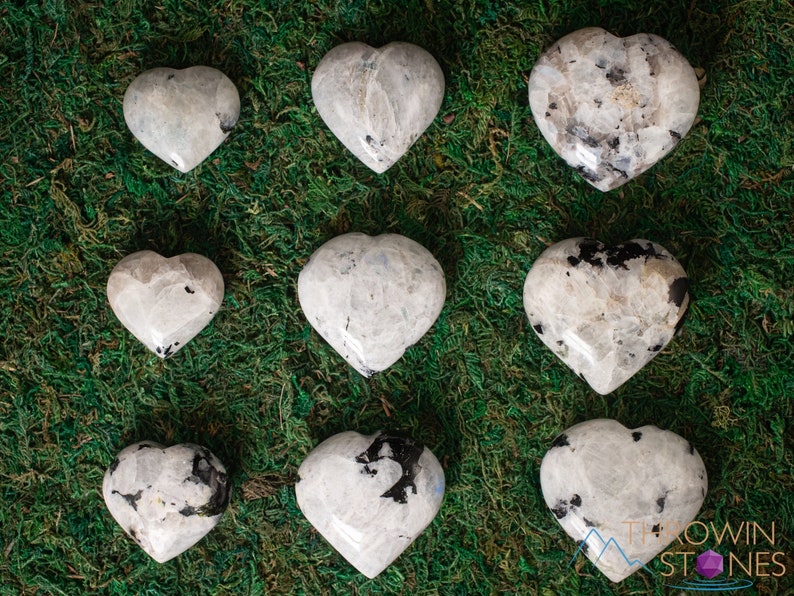 Genuine Moonstone heart shaped crystal. This beautifully hand carved, puffy, palm stone heart, is white with specks of black and rainbow flash. Each crystal heart is unique, and has its own color, shape, and pattern. This listing has variations.