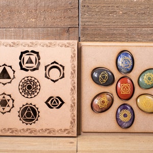 May include: Wooden box with seven chakra stones, each with a different color and symbol. The stones are arranged in a circle and are surrounded by a wooden frame. The box also includes a wooden panel with seven chakra symbols.