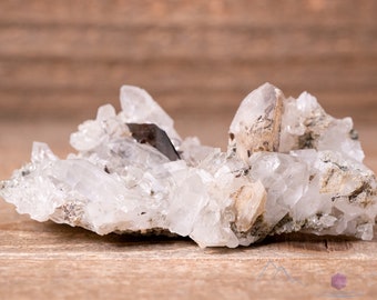 May include: A cluster of clear quartz crystals with a single, larger crystal in the center. The crystals are embedded in a matrix of gray rock.