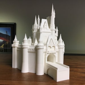 Puede incluir: Un modelo blanco de castillo de Cenicienta de Disney World impreso en 3D. El castillo tiene un diseño detallado con torres, chapiteles y un puente levadizo.