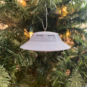 May include: A gray UFO-shaped Christmas ornament hanging on a green Christmas tree.