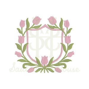 May include: An embroidery design featuring a central shield outline framed by a wreath of light pink tulips with green stems and leaves. The design includes a faint, stylized monogram overlay in the center and light script text at the bottom.
