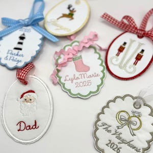 Può includere: Ornamenti natalizi ricamati con vari disegni, tra cui un faro, una renna, Babbo Natale, una calza, un monogramma e fedi nuziali. Ogni ornamento ha un nastro per appenderlo e testo personalizzato.