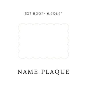 May include: A white, scalloped-edge name plaque. The text "5X7 HOOP - 6.9X4.9" is at the top, and "NAME PLAQUE" is at the bottom. The plaque is designed for embroidery or personalization.
