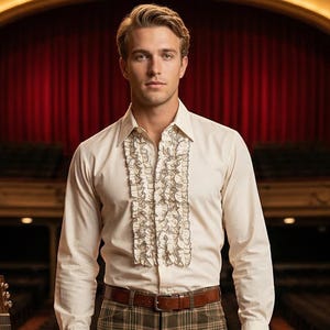 May include: A man in a cream-colored shirt with ruffled detailing, brown plaid pants, and brown boots stands on a stage. A brown leather belt and a guitar on a stand are also visible. The background features a theater setting.
