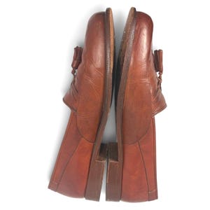 May include: A pair of brown leather tassel loafers featuring a rounded toe, a low stacked heel, and decorative stitching along the vamp. The shoes have a smooth finish with visible natural creasing on the upper surface and a dark brown sole.