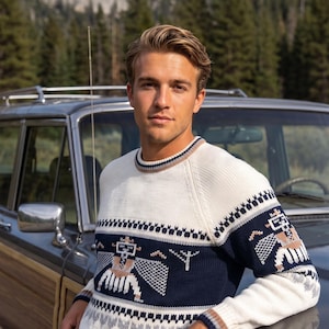 May include: A long-sleeve crewneck sweater featuring a cream-colored base with a prominent navy blue horizontal band across the chest and sleeves. The sweater displays a geometric bird-like motif in white, tan, and grey, with striped trim.