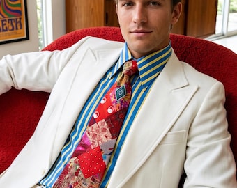 May include: A white blazer and matching trousers worn with a blue and yellow striped button-down shirt and a multi-coloured patchwork tie featuring various red, pink, and patterned fabric squares with a small central geometric emblem.