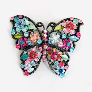 May include: A colourful butterfly brooch with a metal frame and a floral design. The butterfly is adorned with pink, blue and green crystals.