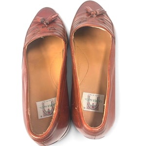 May include: A pair of brown leather loafers featuring a tassel detail on the top of each shoe. The interior of the shoes includes a white label with the text Cable & Co. and Made in Italy printed in black, visible inside the heel area.