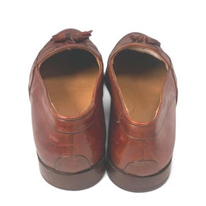 May include: A pair of brown leather loafers featuring a tassel detail on the top. The shoes have a smooth finish, a rounded toe, and a low heel. The interior is lined with a tan material, and the soles are constructed from a dark brown material.