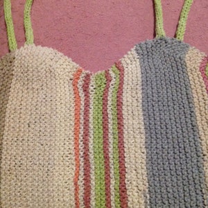 Könnte beinhalten: Eine gestreifte Stricktasche mit grünen, rosa und orangen Streifen. Die Tasche hat zwei grüne Henkel.