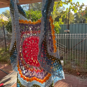 May include: A crocheted vest with a rainbow pattern. The vest is made of a light blue yarn with accents of red, orange, yellow, green, purple, and pink.