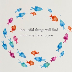Peut inclure: Une carte de vœux blanche présentant une disposition circulaire de petits poissons aquarelles colorés dans des tons de bleu, orange, rose et sarcelle. Le centre du cercle contient le texte noir : beautiful things will find their way back to you.
