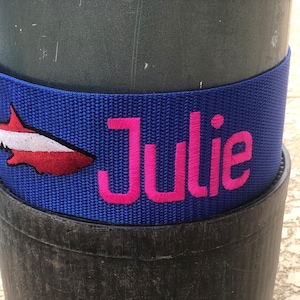 May include: Blue scuba tank strap with a red and white fish design and the name "Julie" embroidered in pink.