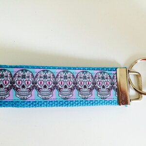 May include: A blue and pink key chain with a repeating pattern of sugar skulls. The key chain has a silver metal ring.