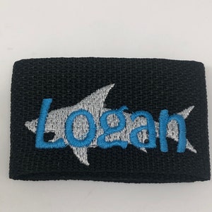 May include: Black fabric patch with a white shark silhouette and the name "Logan" embroidered in blue.