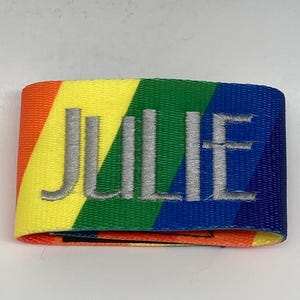 May include: A rainbow-colored fabric wristband with the name "JULIE" embroidered in silver thread.
