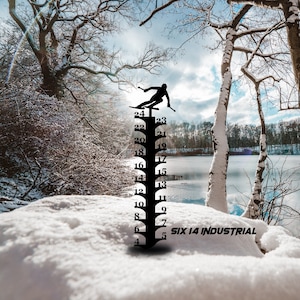 May include: Black metal snow gauge with a skier silhouette at the top and numbered increments from 4 to 24. The text "SIX 14 INDUSTRIAL" is at the bottom. The gauge is set in a snowy landscape.