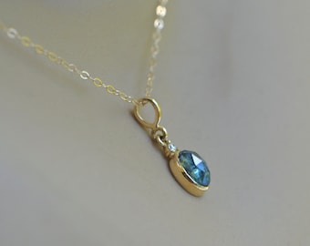May include: A delicate gold chain necklace with a small oval-shaped pendant featuring a blue gemstone and a tiny diamond accent.