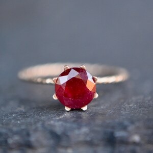 May include: A close-up of a ring with a red ruby gemstone set in a gold band.