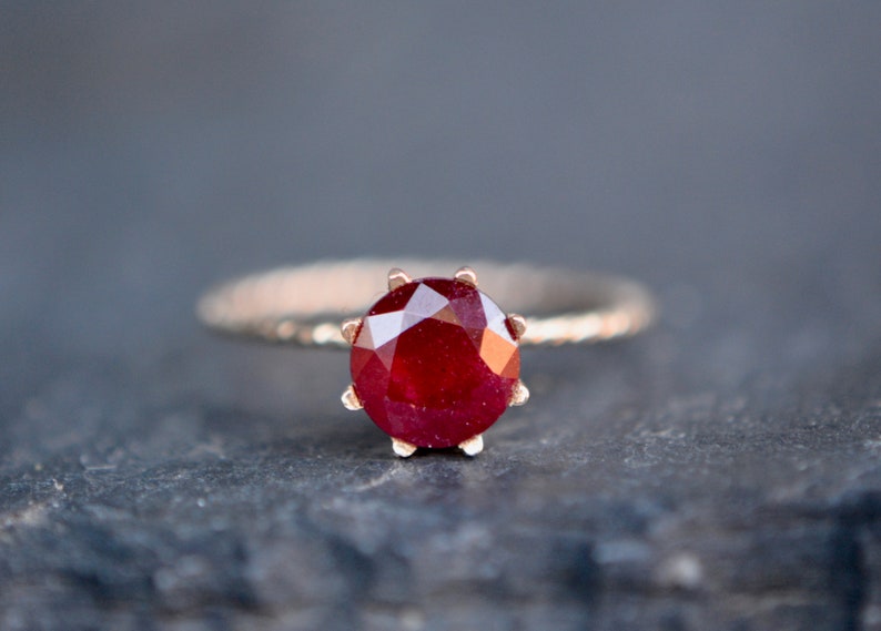 May include: A close-up of a ring with a red ruby gemstone set in a gold band.