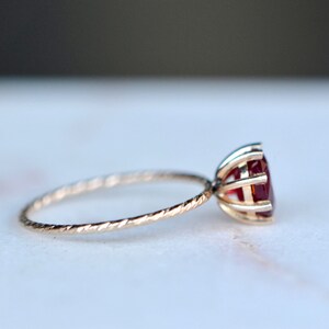 May include: A delicate gold ring with a twisted band and a red gemstone set in a cage-like setting.
