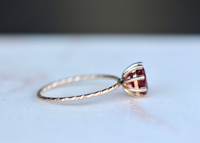 May include: A delicate gold ring with a twisted band and a red gemstone set in a cage-like setting.