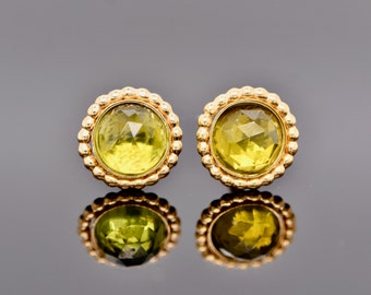 May include: A pair of round stud earrings featuring faceted, translucent lime-green stones set in gold-toned metal frames with a beaded, textured border. The earrings are circular and display a reflective, polished finish on the metal edges.
