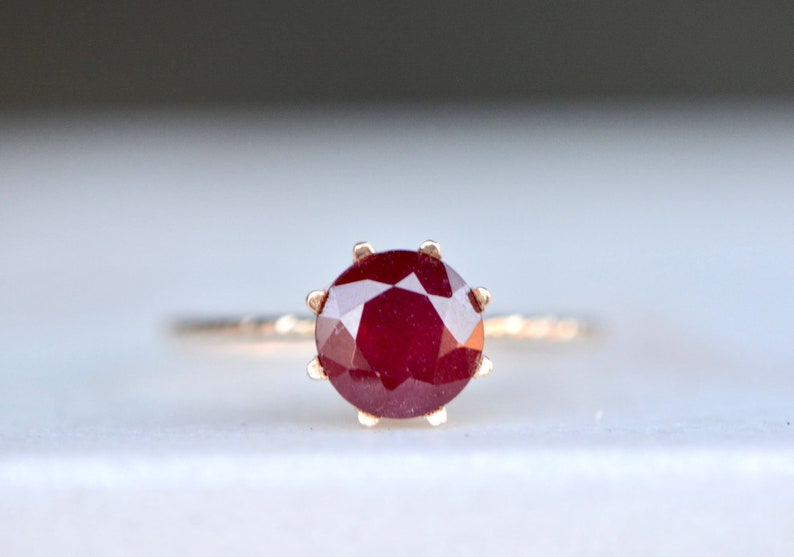 May include: A close-up of a ruby ring with a gold band. The ruby is a deep red color and has a faceted cut.