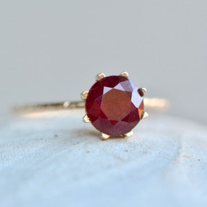 May include: A gold ring with a red ruby gemstone set in a prong setting.