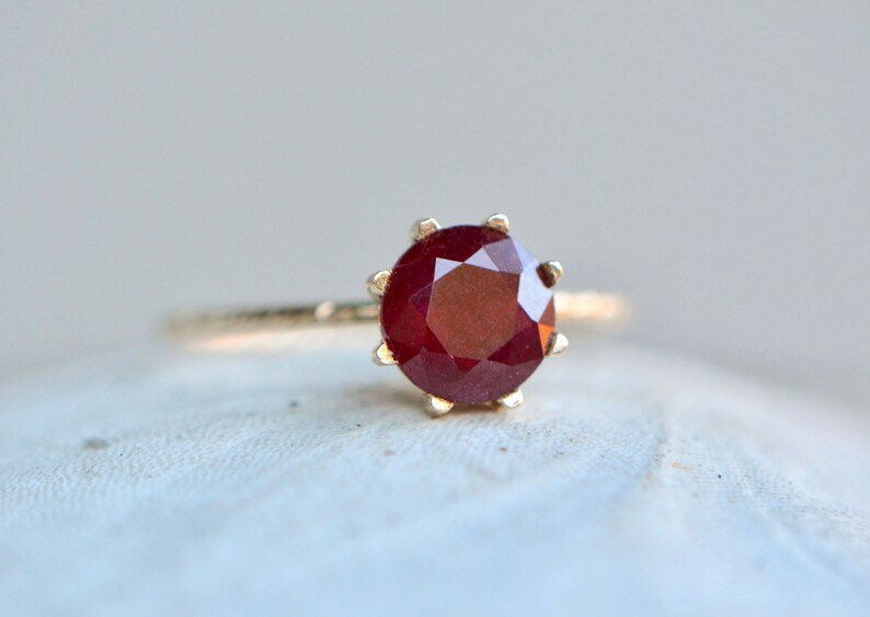 May include: A gold ring with a red ruby gemstone set in a prong setting.