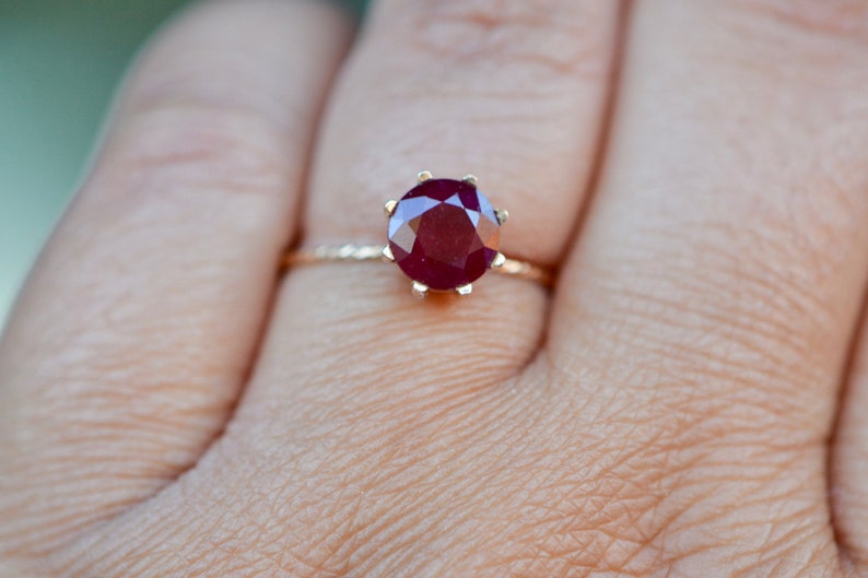 May include: A gold ring with a large, round, red ruby gemstone set in a prong setting.
