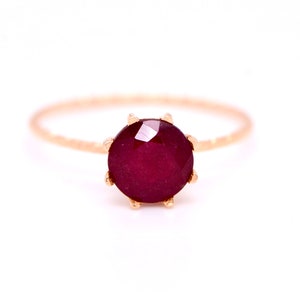 May include: A delicate gold ring with a deep red gemstone set in a prong setting.