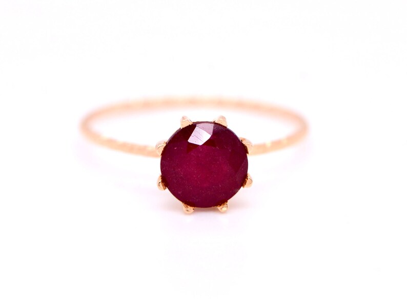 May include: A delicate gold ring with a deep red gemstone set in a prong setting.
