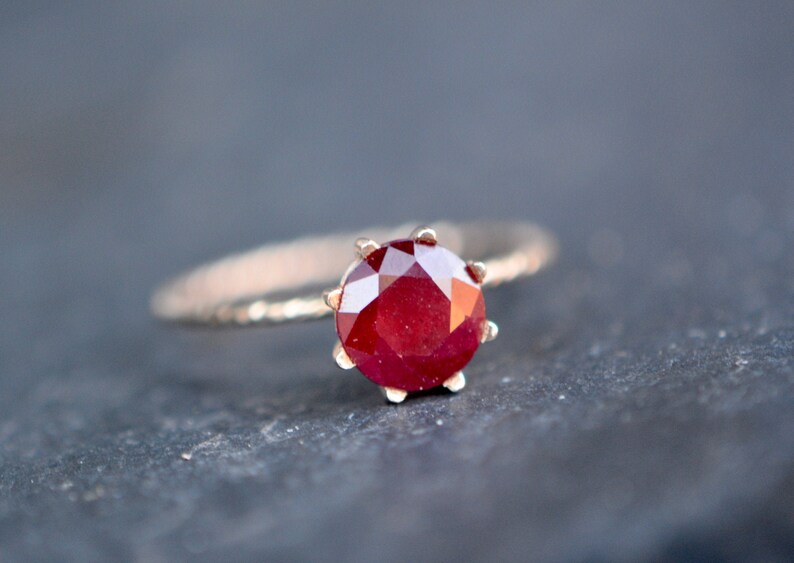 May include: A gold ring with a red ruby gemstone set in a prong setting.