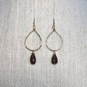 May include: A pair of gold earrings with a teardrop-shaped smoky quartz gemstone dangling from each earring.