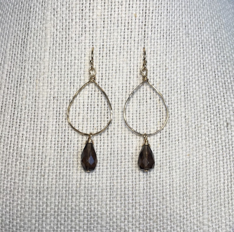 May include: A pair of gold earrings with a teardrop-shaped smoky quartz gemstone dangling from each earring.