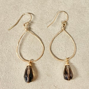 May include: Gold teardrop earrings with smoky quartz gemstone drops. The earrings have a hammered wire design.