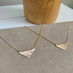 May include: Two gold necklaces with triangular pendants. One pendant is plain and the other has a floral design.