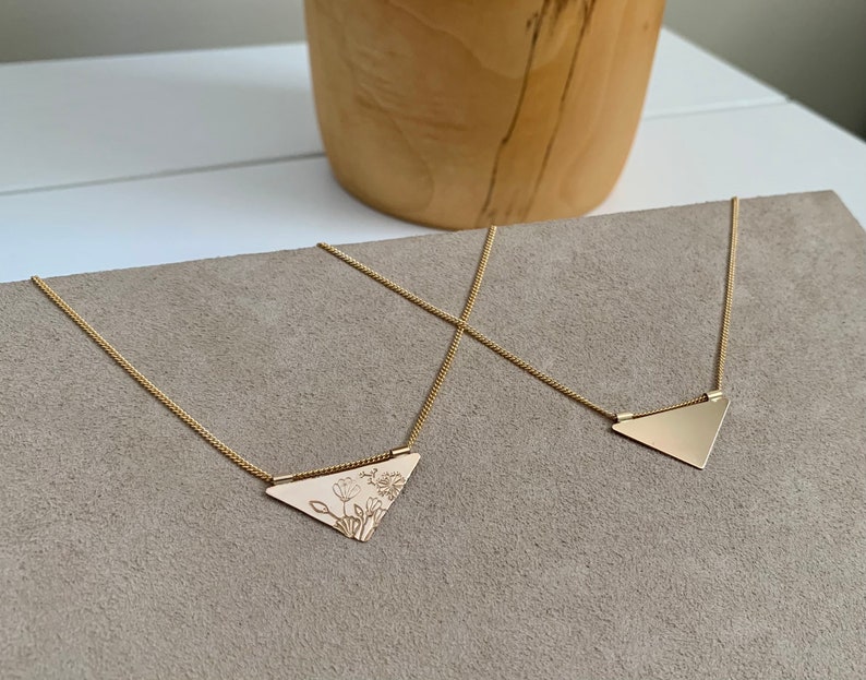 May include: Two gold necklaces with triangular pendants. One pendant is plain and the other has a floral design.