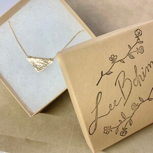 May include: A gold triangle pendant necklace in a brown box with the text "Lee Bohmi" on the lid.