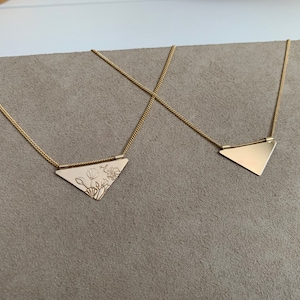 May include: Two gold necklaces with triangular pendants. One pendant features a floral design, while the other is plain.