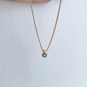 Puede incluir: Un delicado collar de cadena de oro con un pequeño colgante redondo de piedra preciosa azul claro.