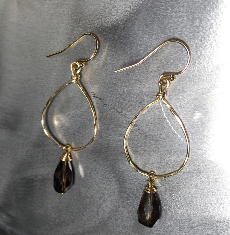 May include: Gold teardrop earrings with a dark brown gemstone pendant. The earrings are made of wire and have a delicate, hammered finish.